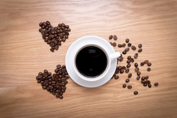 Hot cup of espresso and heart shape made from coffee beans on wooden surface.