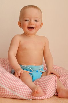 Happy baby having blue cloth nappy sitting on pillow. Child concept.