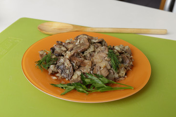 Fried mushrooms with onions and spices in an orange dish decorated with dill and parsley
