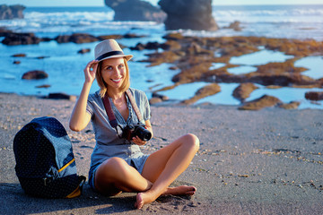 Fototapeta na wymiar Travel and hobby. Pretty young woman with camera and rucksack on the ocean beach.