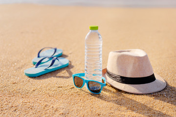 Vacation concept. Essentials on the sea beach. Bottle of drinking water, sunglasses, hat, flip-flops.