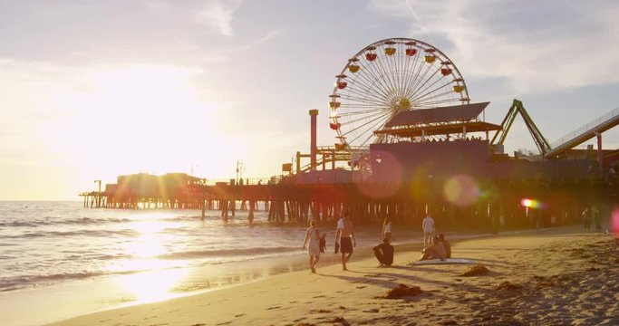 People relaxing on the beach next to the Santa Monica Pier during sunset.