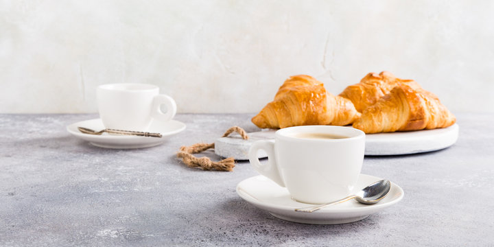 White cups of coffee and croissants on light gray background, selective focus. Healthy breakfast concept with copy space.
