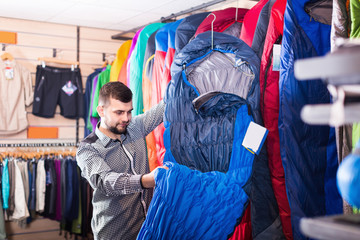 Guy choosing new sleeping bag in sports shop