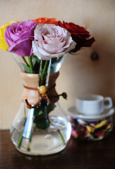 Colored roses in a coffee pot and white cup on a stand with dried flowerson on wooden background