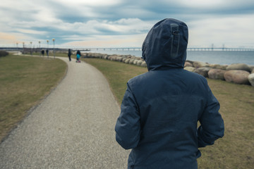 Lonely hooded female person from behind standing at seashore