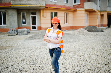 Engineer builder woman in uniform waistcoat and orange protective helmet against new building....