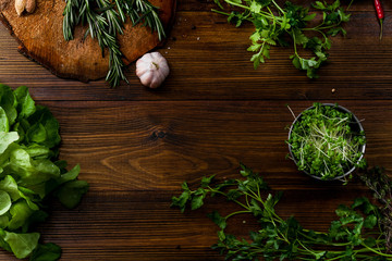 Fresh salad ingredients, herbs, tomatoes and garlic on wooden background. Top view with text space. Organic concept.