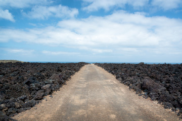 Fototapeta na wymiar Track road among the rocks of lava in Timanfaya national park in Lanzarote, Canary Islands, Spain