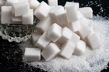 white granulated sugar and refined sugar on black tables surface, closeup