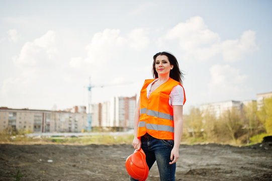 Engineer builder woman in uniform waistcoat and orange protective helmet against new buildings.