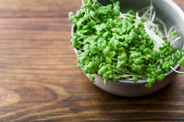 Mustard microgreen salad in metallic bowl on wooden background