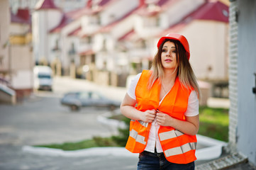 Engineer builder woman in uniform waistcoat and orange protective helmet against new building. Property living block theme.