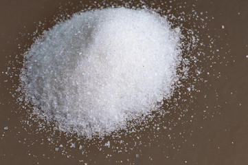 Heap of white granulated sugar on gray surface. Close-up