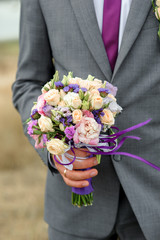A stylish bridal bouquet of fresh flowers with an accent purple in the hand of the groom
