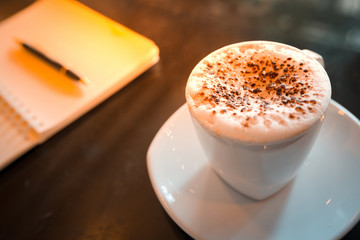 Cappuccino coffee,notebook and pen on table in the morning