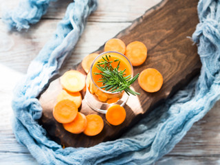 Orange carrot juice on wooden board with rosemary. Summer smoothie breakfast diet refreshment