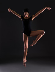 beautiful woman ballerina in black body suit jumping over black