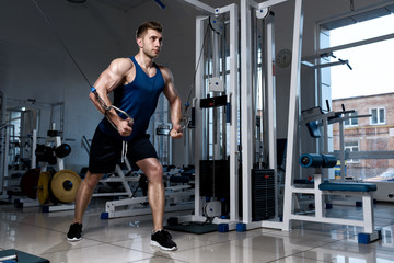 Fototapeta na wymiar Athletic man in a T-shirt standing training on a exercise machine in the gym