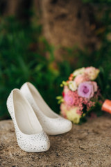 bride's shoes lie on the green grass in the forest next to a wedding bouquet of flowers and greenery