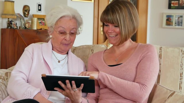 Seniorin mit Tochter/Enkelin/Betreuerin und Tablet Computer