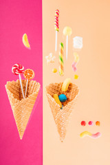 waffle cones with different delicious jelly candies and lollipops on pink and beige