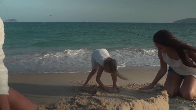 Happy mother and daughters build a sand castle on the beach of the South China Sea slow motion stock footage video