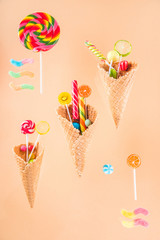 waffle cones with different delicious jelly candies and lollipops on beige