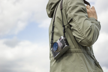 Old camera hanging on the shoulder of a person in a jacket with a hood on a cloudy sky background