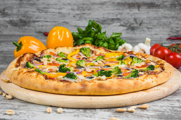 Vegetarian pizza with rosemary and spices on a light wooden background. Italian pizza on a background of green basil and fresh vegetables