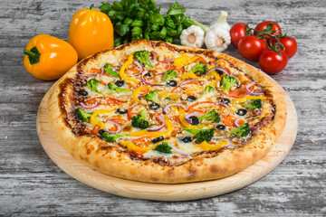 Vegetarian pizza with rosemary and spices on a light wooden background. Italian pizza on a background of green basil and fresh vegetables