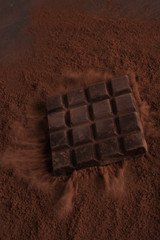 Dark chocolate bar falling in chocolate powder