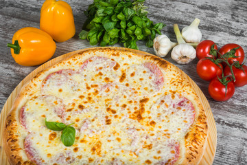 Pizza with ham under cheese, with rosemary and spices on a light wooden background. Italian pizza on a background of green basil and fresh vegetables