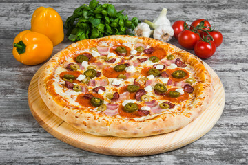 Pizza with smoked meat, with rosemary and spices on a light wooden background. Italian pizza on a background of green basil and fresh vegetables