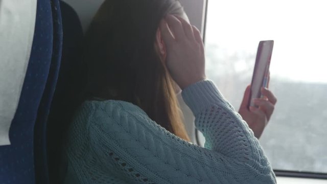 Girl looking into the phone as mirror for ombing her hair during travelling on railroad. Beautiful woman rides on the train, looking at smartphone and correct his hairstyle. Female doing selfie