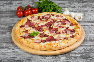 Pizza with smoked meat, with rosemary and spices on a light wooden background. Italian pizza on a background of green basil and fresh vegetables
