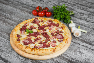 Pizza with smoked meat, with rosemary and spices on a light wooden background. Italian pizza on a background of green basil and fresh vegetables