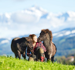 Young woman with two mini Shetland ponies. Two horses and beautiful lady outdoor on mountain background. Horse rider.