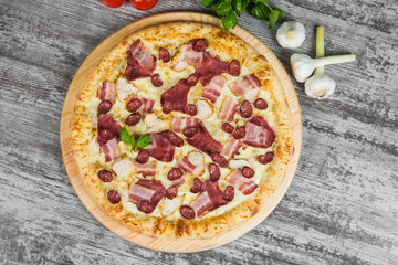 Pizza with smoked meat, with rosemary and spices on a light wooden background. Italian pizza on a background of green basil and fresh vegetables
