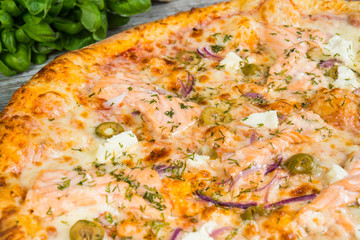 Pizza with salmon (red fish), with rosemary and spices on a light wooden background. Italian pizza on a background of green basil and fresh vegetables