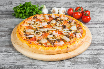 Italian pizza on a light wooden table on the background of vegetables and greens
