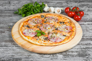 Thin pizza with mushrooms, ham and cheese, rosemary and spices on a light wooden background. Italian pizza on a background of green basil and fresh vegetables