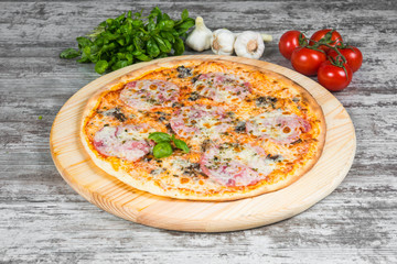 Thin pizza with mushrooms, ham and cheese, rosemary and spices on a light wooden background. Italian pizza on a background of green basil and fresh vegetables