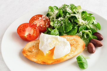 breakfast set of pan fried toast with poached egg, cut tomato, kalamata olives, and green salad dressed with olive oil and lemon juice and sprinkled with grated cheese