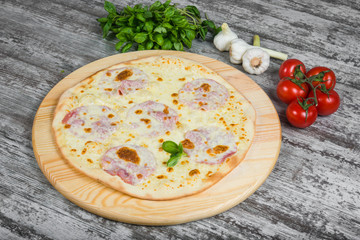 Thin pizza with ham, rosemary and spices on a light wooden background. Italian pizza on a background of green basil and fresh vegetables