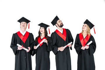 Group of young men and women in graduation gowns and mortarboards holding diplomas