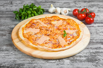 Thin pizza with salmon (red fish), rosemary and spices on a light wooden background. Italian pizza on a background of green basil and fresh vegetables