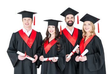 Group of young men and women in graduation gowns and mortarboards holding diplomas