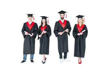 Full length front view of happy students in graduation caps holding diplomas on white