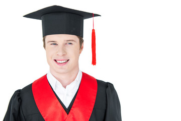 Portrait of happy young man in academic gown and mortarboard smiling on white